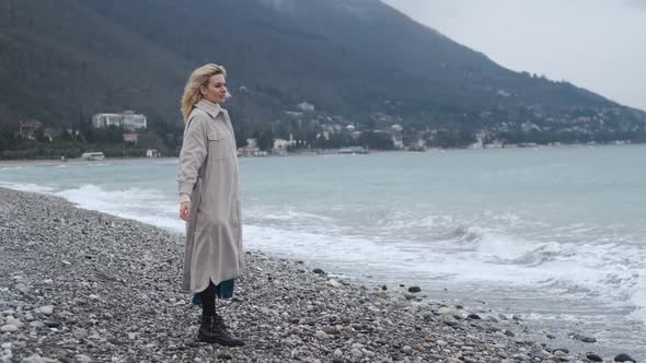 a slender woman in a coat enjoys the sea air on the beach