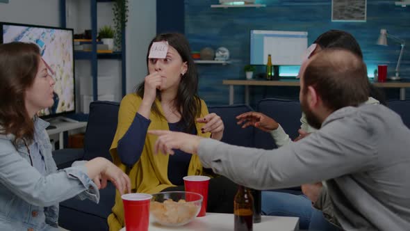 Mixed Race Friends Playing Guess Who Game with Sticky Papers Attached on Forehead alt