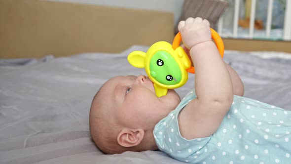 Happy Baby Girl Plays with Colorful Toy on Large Bed alt