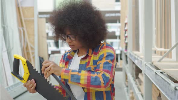 African American Woman with an Afro Hairstyle in the Store Chooses a Saw for Repair alt