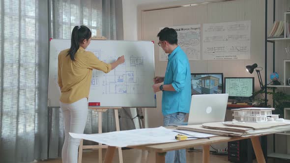 Asian Woman And Man Engineers With Blueprint On Whiteboard Discuss About Design At The Office alt