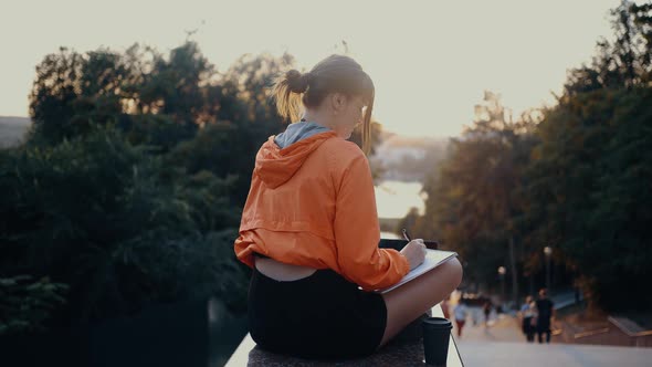 The Young Woman Filmed From Behind Working on Her Laptop and Taking Notes in Her Notebook the Young alt