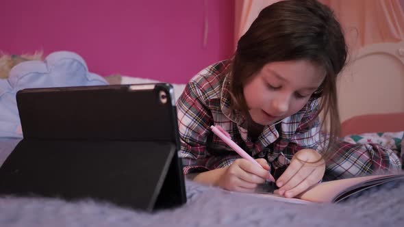 Distance education at home, online e-learning. Cute child is looking in laptop screen lying on bed 