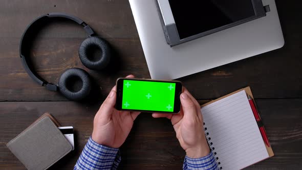 Hands of Man Using Smartphone with Green Screen on Wood Table alt