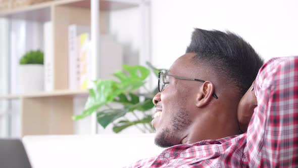 Happy African man feels relaxing on sofa in break time from work alt