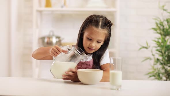Child Pours Milk Into a Bowl of Cereal in the Kitchen