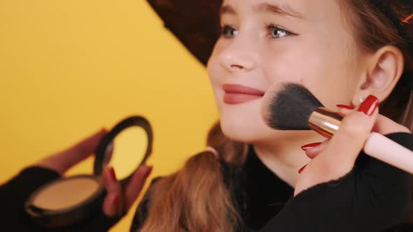 Woman Applyng Makeup on Girl's Face on Orange Background alt
