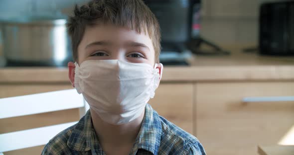 Small boy in quarantine at home look at camera in blue medical mask