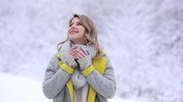 Beautiful woman in coat with cup of hot drink in a snow forest.
