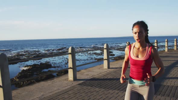African american woman in sportswear running on promenade by the sea alt