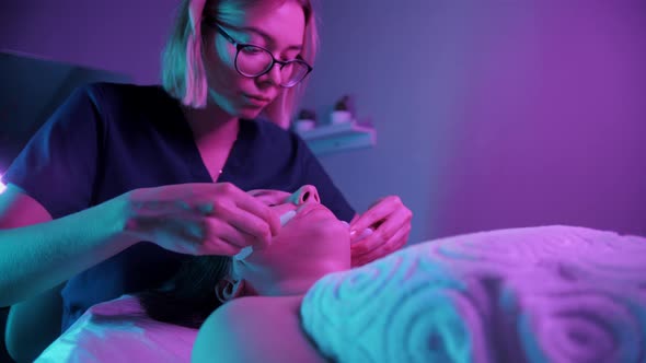 Massage Session  Young Blonde Woman Using Jade Stones on the Face of Her Female Client alt