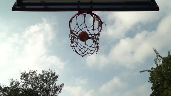 Thrown Orange Basketball Hits the Basket on an Outdoor Court in the Shade of Trees alt