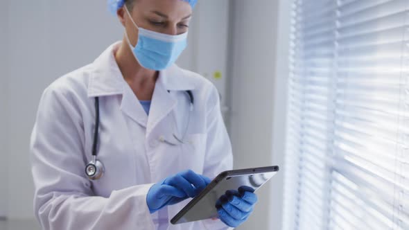 Caucasian female doctor wearing face mask and surgical gloves using tablet alt