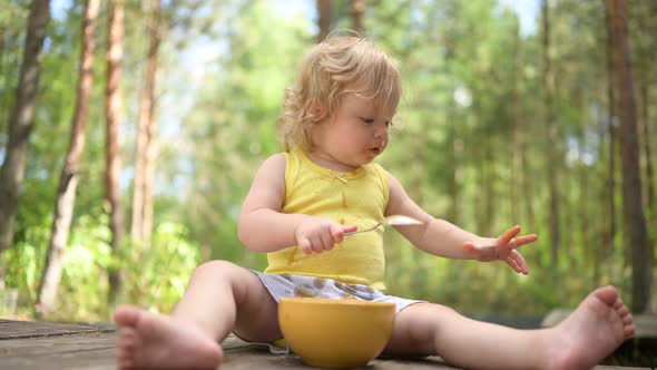Little Funny Cute Blonde Girl Child Toddler with Dirty Clothes and Face Eating Baby Food Fruit or alt