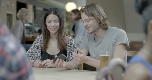 Man holding mobile phone and talking with woman while sitting in pub