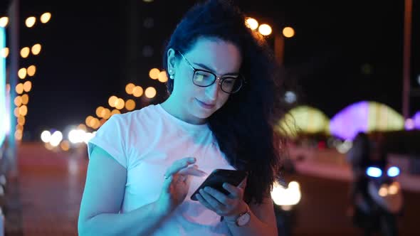 Pretty Woman Stands on the Street in a White T-shirt and Glasses, Makes Online Payments By Credit alt