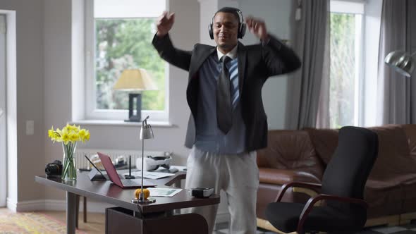 Joyful African American Young Man in Headphones Dancing in Home Office Indoors alt