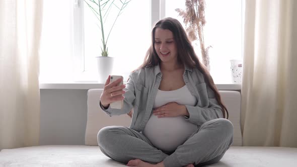 Happy Pregnant Woman with Tablet Have Video Call Using Smartphone Communicates with Husband Via Chat