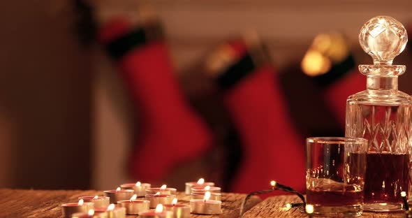 Whisky decanter, tealight candle and christmas lights on plank alt
