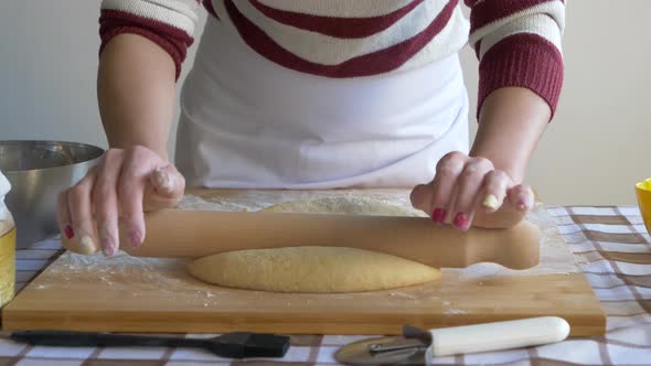 Woman flattening pastry dough with rolling pin on baking board