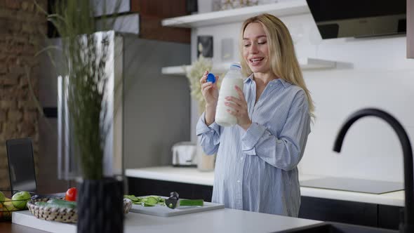 Portrait of Happy Pregnant Caucasian Woman Smelling Milk Smiling Standing in Kitchen at Home alt