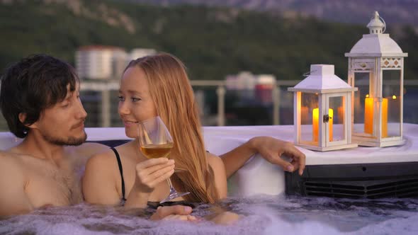 A Young Man and Woman are Relaxing in the Hot Tub on a Rooftop with a View on Mountains During alt