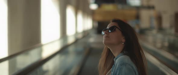 Woman with sunglasses looking around while standing on a moving walkway alt