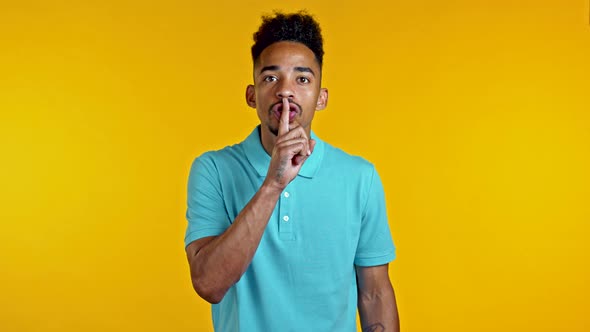 Serious African American Man Holding Finger on Lips Over Yellow Background. Gesture of Shhh, Secret alt