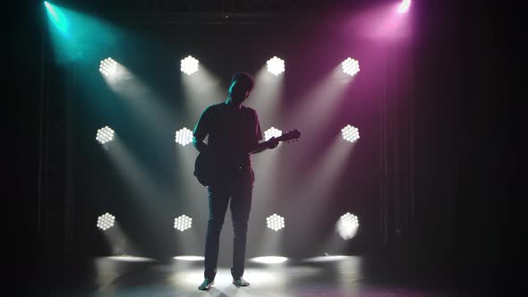 African Folklore. A Barefoot Man Plays the Guitar in a Dark Studio Against the Backdrop of Bright alt