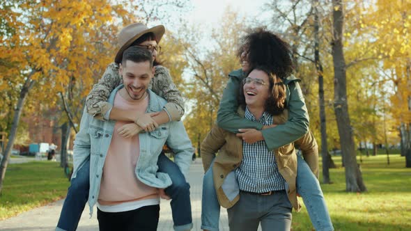 Portrait of Happy Guys Friends Giving Piggyback Ride To Girls Laughing in City alt