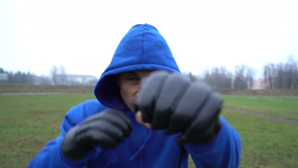 Man Sportsman Boxer Guy Wearing Boxing Gloves Training Outdoors, Doing Punches In, Man in a Hood