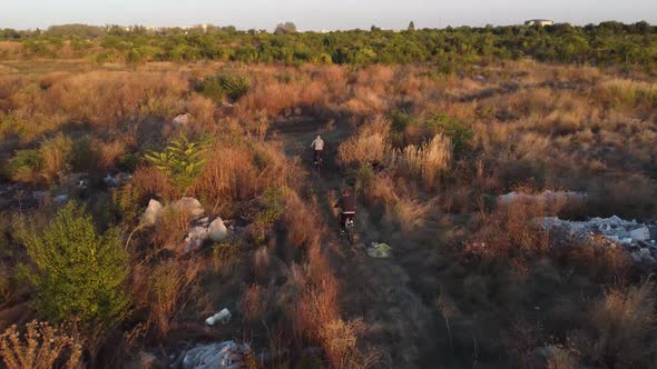 Aerial View of 2 Bikers Riding a Path Full of Waste Garbage Land Close to a City