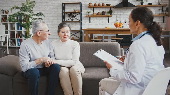 Doctor Woman Announcing Good Test Results to an Elderly Couple Who Rejoicing Sitting on Couch During alt
