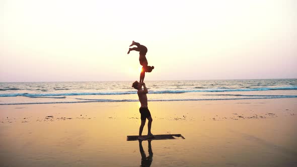 Fit Sporty Couple Practicing Acro Yoga with Partner Together on the Sandy Beach alt