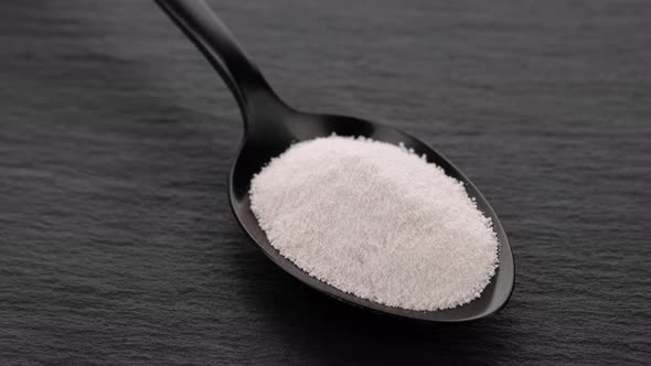 Collagen powder peptide in black spoon on black stone alt