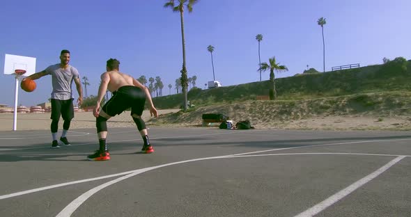 A man dribbles while playing one-on-one basketball hoops on a beach court alt