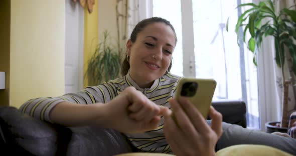 Happy woman using mobile phone on the sofa and enjoying a funny chat with fri