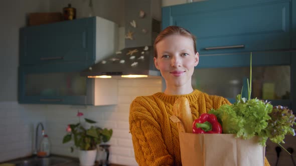 Beautiful Woman with Groceries Bag in Hands at Kitchen Looks Camera Smiling alt