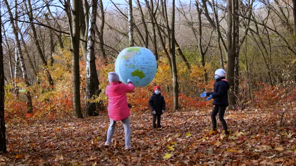 Two girls and a small boy in medical masks play in the autumn Park with a large inflatable ball