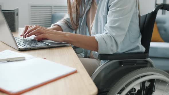 Unrecognizable Disabled Girl Using Laptop Typing Sitting in Wheelchair at Desk Busy with Online Work alt