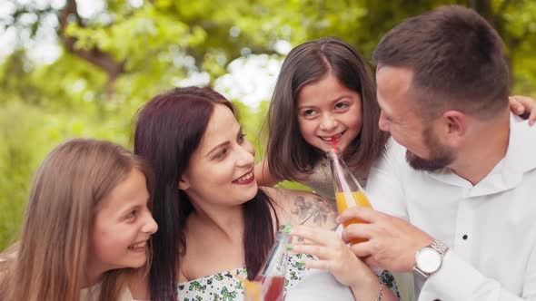 Smiling Father Mother and Two Cute Daughters Drinking Fresh Juice at Green alt