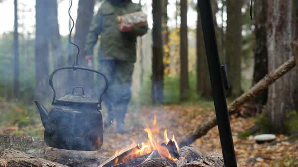 Camping Kettle over Burning Fire and a Hiker with Firewood alt