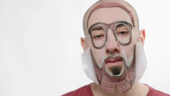 Closeup Portrait of a Man with a Fabric Moisturizing Mask on His Face with a Print of a Beard and alt