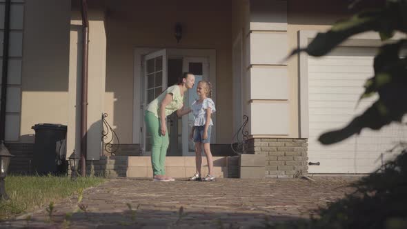 Beautiful Young Mother Lets Her Daughter Go for a Walk with Friends Kissing Her on the Cheek alt