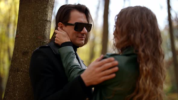a Blonde in a Green Jacket Strokes a Man's Hair and Takes Off His Sunglasses in an Autumn Park on a alt