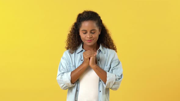 Portrait of smiling young African American woman thank god and praying with hands clasped