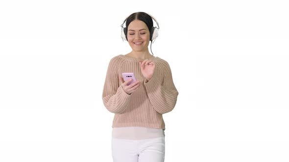 Happy Girl Walking Listening To Music with Smart Phone Wearing Headphones on White Background. alt