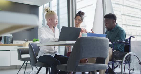 Diverse business people discussing with disabled colleague and documents in creative office alt