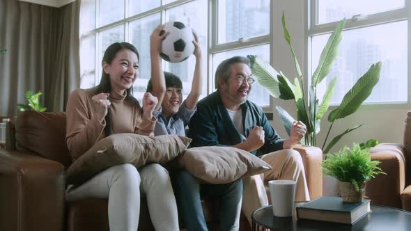 Asian parents And Son Watching Sports On TV Cheering Favorite Soccer Team alt