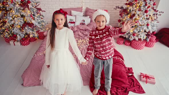 Portrait of Attractive Cute Kids Wearing Christmas Wear Falling Together on Bed in Apartment alt